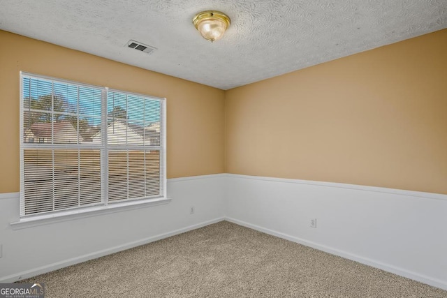 spare room featuring a textured ceiling, carpet, visible vents, and baseboards