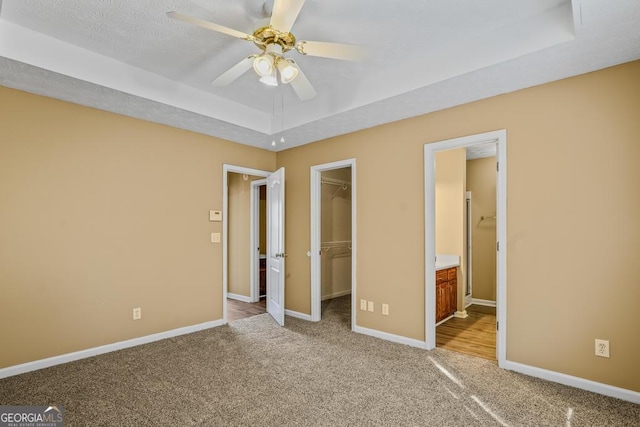 unfurnished bedroom with a spacious closet, a tray ceiling, carpet flooring, and baseboards