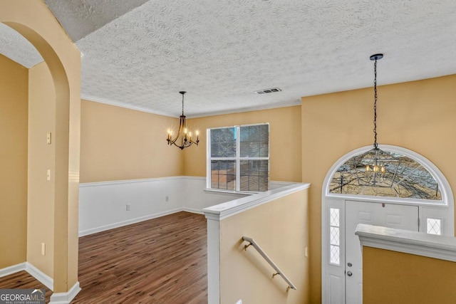 entryway with arched walkways, visible vents, dark wood finished floors, a textured ceiling, and a notable chandelier