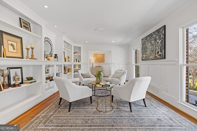 living area with built in features, wood finished floors, recessed lighting, crown molding, and a decorative wall