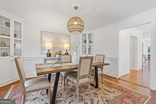 dining room featuring built in shelves, a wainscoted wall, light wood-type flooring, ornamental molding, and a decorative wall