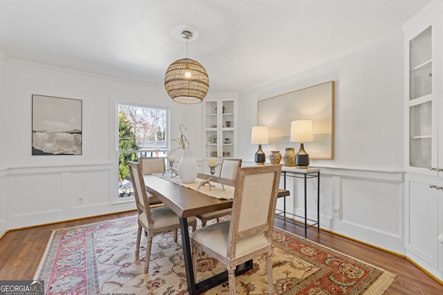 dining space with built in features, wood finished floors, ornamental molding, and wainscoting