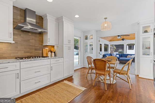 kitchen with ceiling fan, wall chimney range hood, stainless steel gas cooktop, decorative backsplash, and white cabinetry