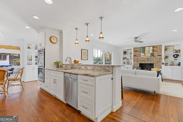 kitchen with light stone countertops, dark wood finished floors, stainless steel appliances, a ceiling fan, and a sink