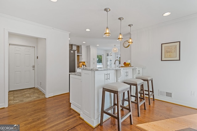 kitchen with a breakfast bar area, visible vents, a peninsula, ornamental molding, and white cabinets