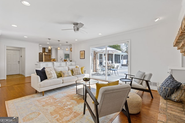 living room featuring baseboards, wood finished floors, ornamental molding, and a ceiling fan