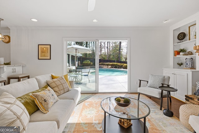 living area featuring recessed lighting, built in shelves, crown molding, and wood finished floors