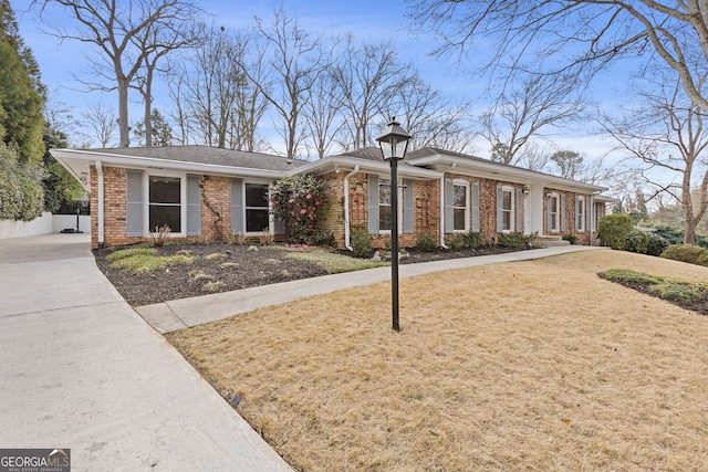 ranch-style house featuring driveway, brick siding, a front yard, and fence