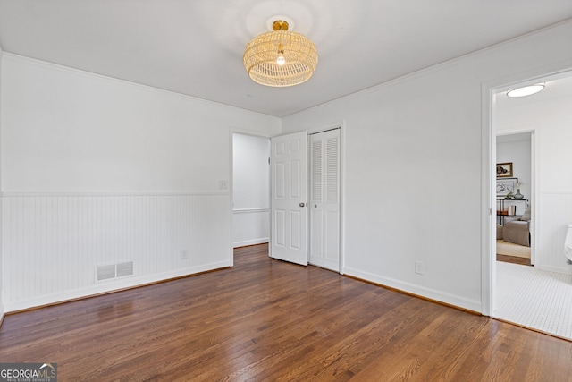 unfurnished bedroom featuring wood finished floors, visible vents, ornamental molding, a closet, and wainscoting