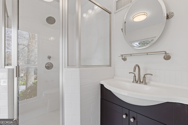 bathroom with visible vents, tile walls, a wainscoted wall, a tile shower, and vanity