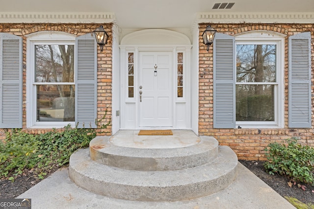 property entrance featuring brick siding and visible vents