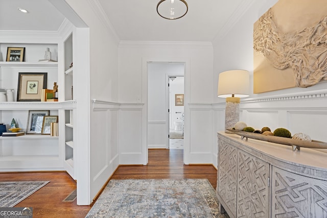 hall featuring built in shelves, wood finished floors, crown molding, and a decorative wall