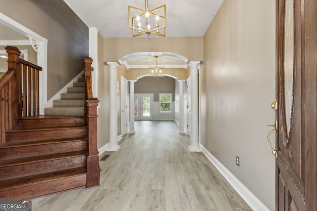 foyer featuring arched walkways, light wood-style floors, a chandelier, ornate columns, and stairs