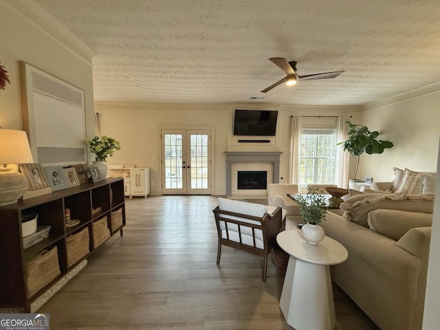 living area with french doors, a fireplace, ornamental molding, a ceiling fan, and wood finished floors