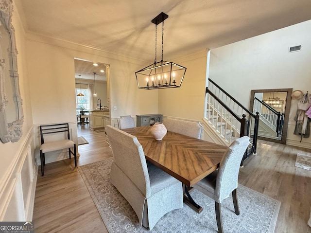 dining room featuring stairway, light wood-type flooring, an inviting chandelier, and crown molding