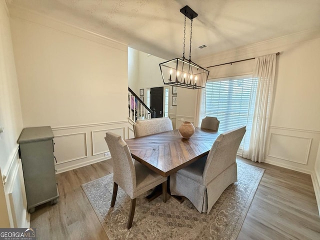 dining area featuring ornamental molding, stairs, a decorative wall, and wood finished floors