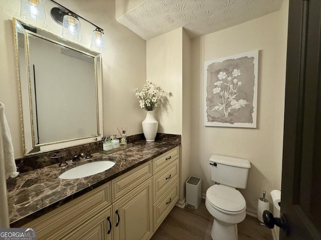 bathroom with toilet, a textured ceiling, vanity, wood finished floors, and baseboards