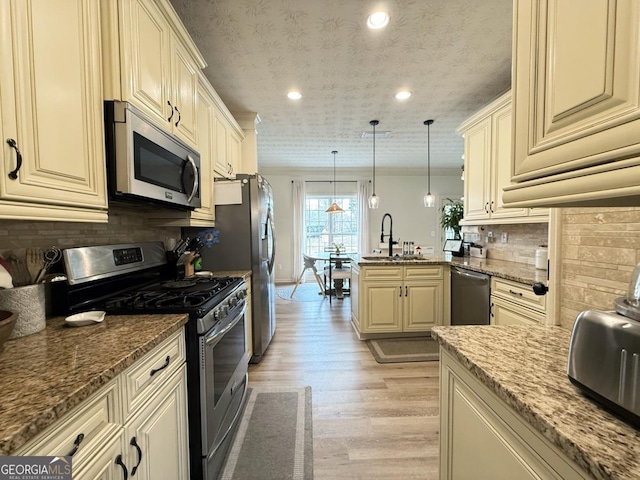 kitchen featuring stainless steel appliances, a peninsula, a sink, cream cabinetry, and tasteful backsplash