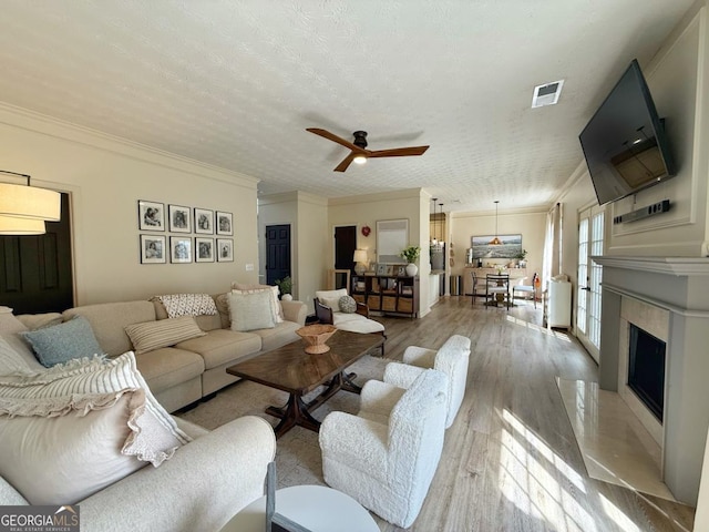 living area featuring light wood-type flooring, a textured ceiling, visible vents, and crown molding