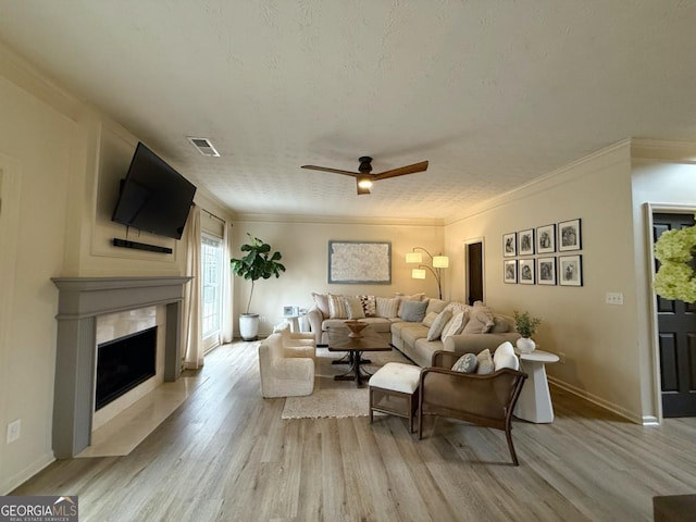 living room featuring ornamental molding, a fireplace, visible vents, and light wood-style floors