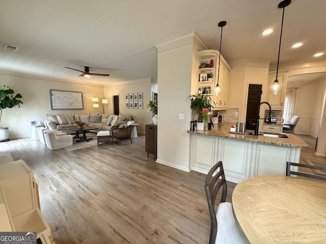 kitchen with visible vents, wood finished floors, a peninsula, crown molding, and a sink