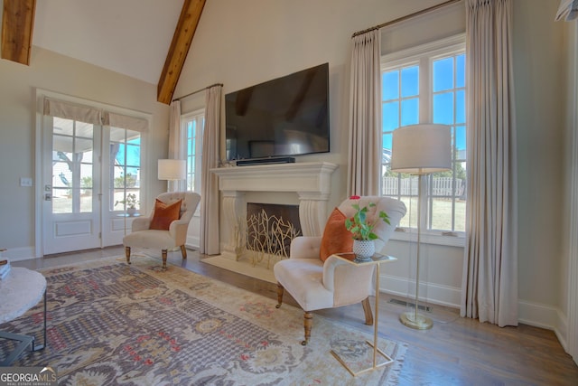 sitting room with a fireplace with flush hearth, vaulted ceiling with beams, baseboards, and wood finished floors