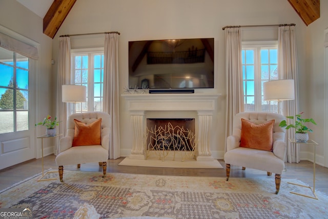 living area featuring lofted ceiling with beams, a fireplace with raised hearth, wood finished floors, and baseboards