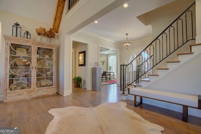 foyer with stairs, ornamental molding, wood finished floors, and an inviting chandelier