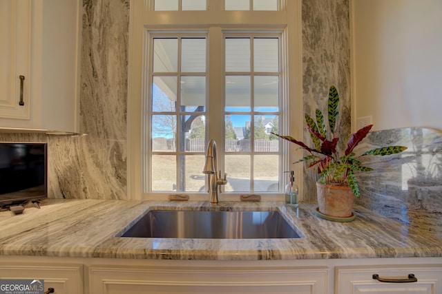 kitchen with white cabinetry, light stone counters, and a sink