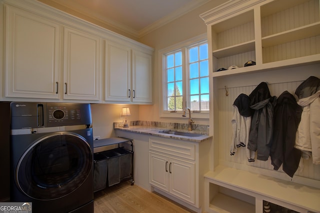 clothes washing area with a sink, ornamental molding, light wood-type flooring, cabinet space, and washer / dryer