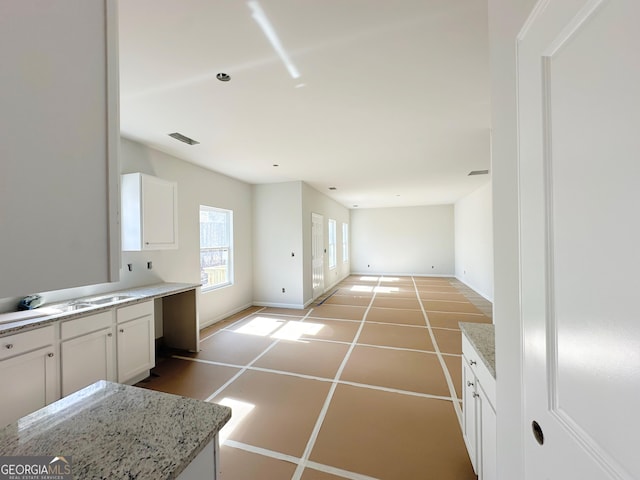 kitchen featuring tile patterned floors, visible vents, baseboards, white cabinetry, and light stone countertops