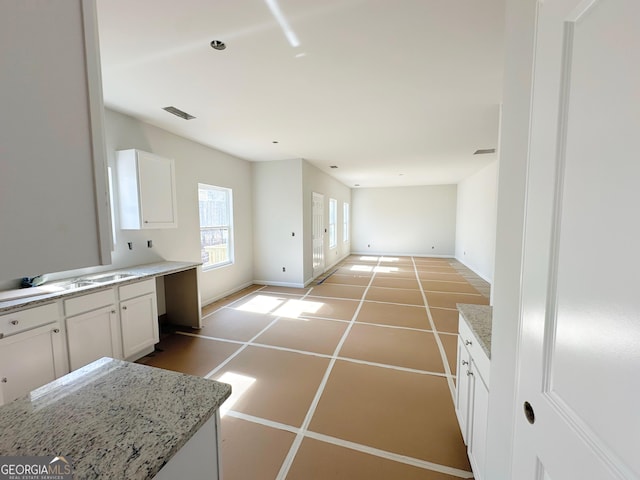 kitchen with visible vents, white cabinets, baseboards, light stone counters, and tile patterned floors