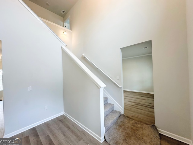 staircase featuring visible vents, a towering ceiling, baseboards, and wood finished floors