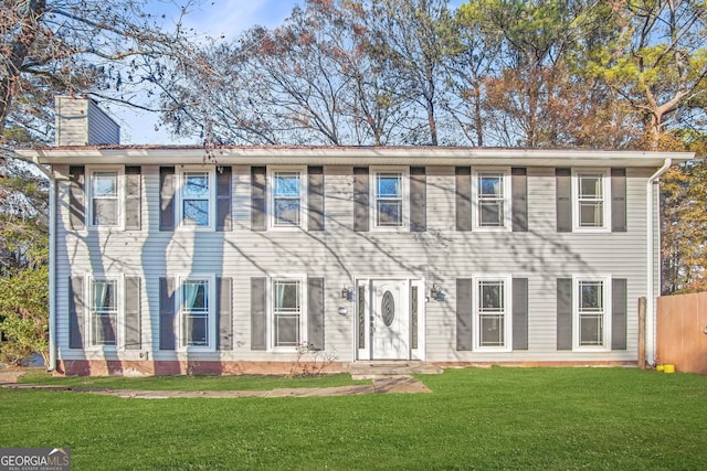 colonial inspired home with a front yard, fence, and a chimney