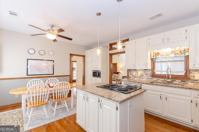 kitchen with stovetop with downdraft, light wood-style flooring, visible vents, a center island, and stainless steel microwave