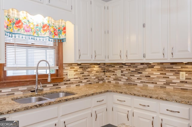 kitchen featuring light stone countertops, white cabinetry, decorative backsplash, and a sink