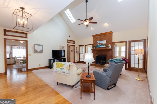 living area featuring high vaulted ceiling, a fireplace, a skylight, baseboards, and light wood-style floors