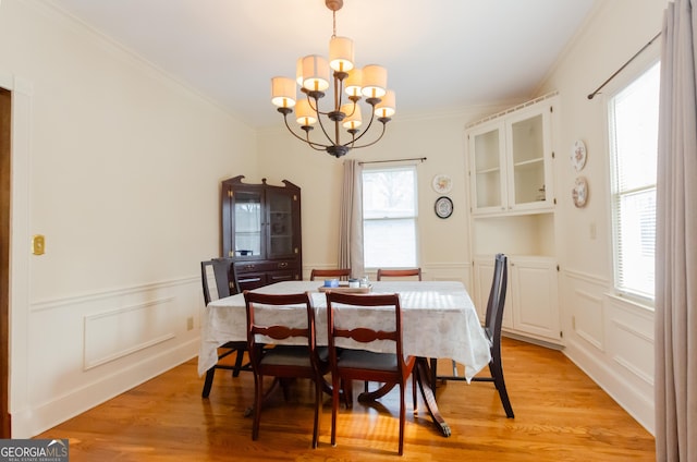 dining space featuring light wood-style floors, ornamental molding, a notable chandelier, and a wainscoted wall