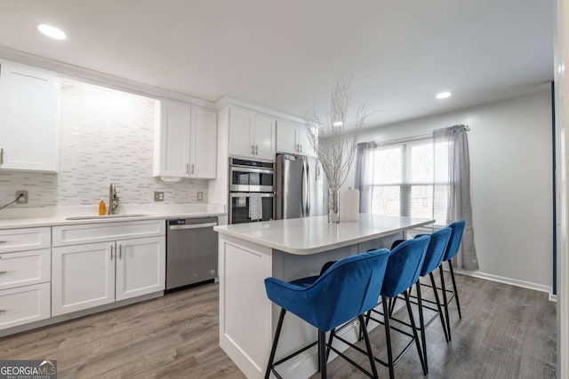 kitchen featuring light wood finished floors, stainless steel appliances, white cabinets, a sink, and a kitchen bar