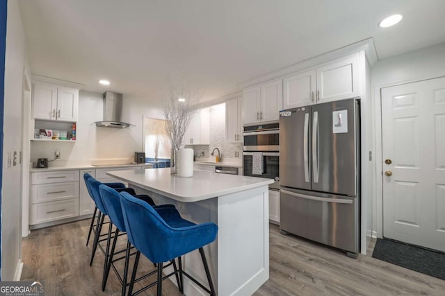 kitchen featuring wall chimney exhaust hood, white cabinetry, stainless steel appliances, and wood finished floors