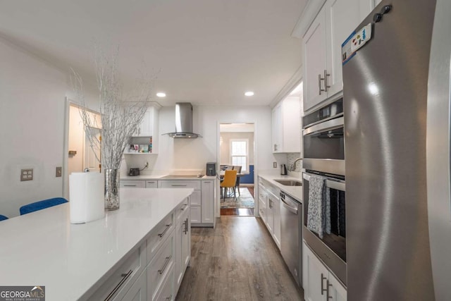 kitchen with stainless steel appliances, light countertops, wall chimney range hood, white cabinetry, and a sink