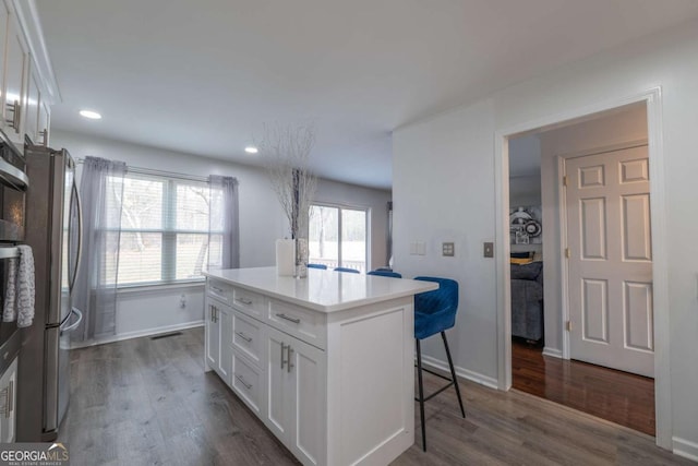 kitchen featuring dark wood-style floors, a breakfast bar area, a center island, freestanding refrigerator, and white cabinetry