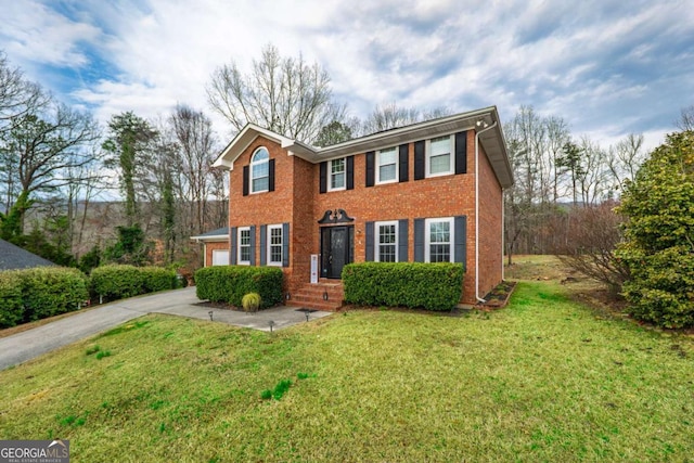 colonial home with driveway, brick siding, and a front yard