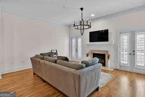 living room with a fireplace with raised hearth, wood finished floors, crown molding, a notable chandelier, and recessed lighting