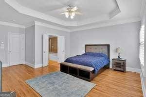 bedroom with light wood finished floors, a raised ceiling, ornamental molding, a ceiling fan, and baseboards