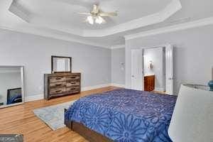 bedroom featuring wood finished floors, a ceiling fan, baseboards, a raised ceiling, and crown molding