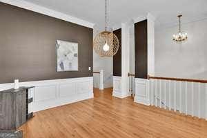 unfurnished dining area featuring wainscoting, a decorative wall, an inviting chandelier, and wood finished floors