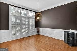 unfurnished dining area featuring ornamental molding, wainscoting, wood finished floors, and a decorative wall