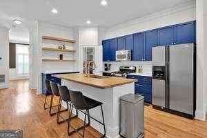 kitchen featuring light wood finished floors, appliances with stainless steel finishes, blue cabinets, a kitchen bar, and a sink