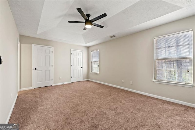 unfurnished bedroom featuring visible vents, baseboards, a raised ceiling, a textured ceiling, and carpet flooring